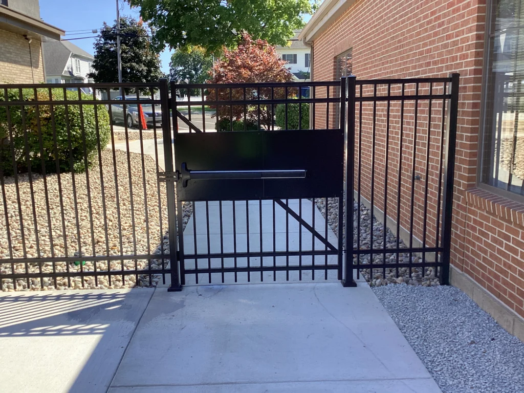 A black ornamental steel security fence with a matching gate featuring an integrated panic bar for emergency exit