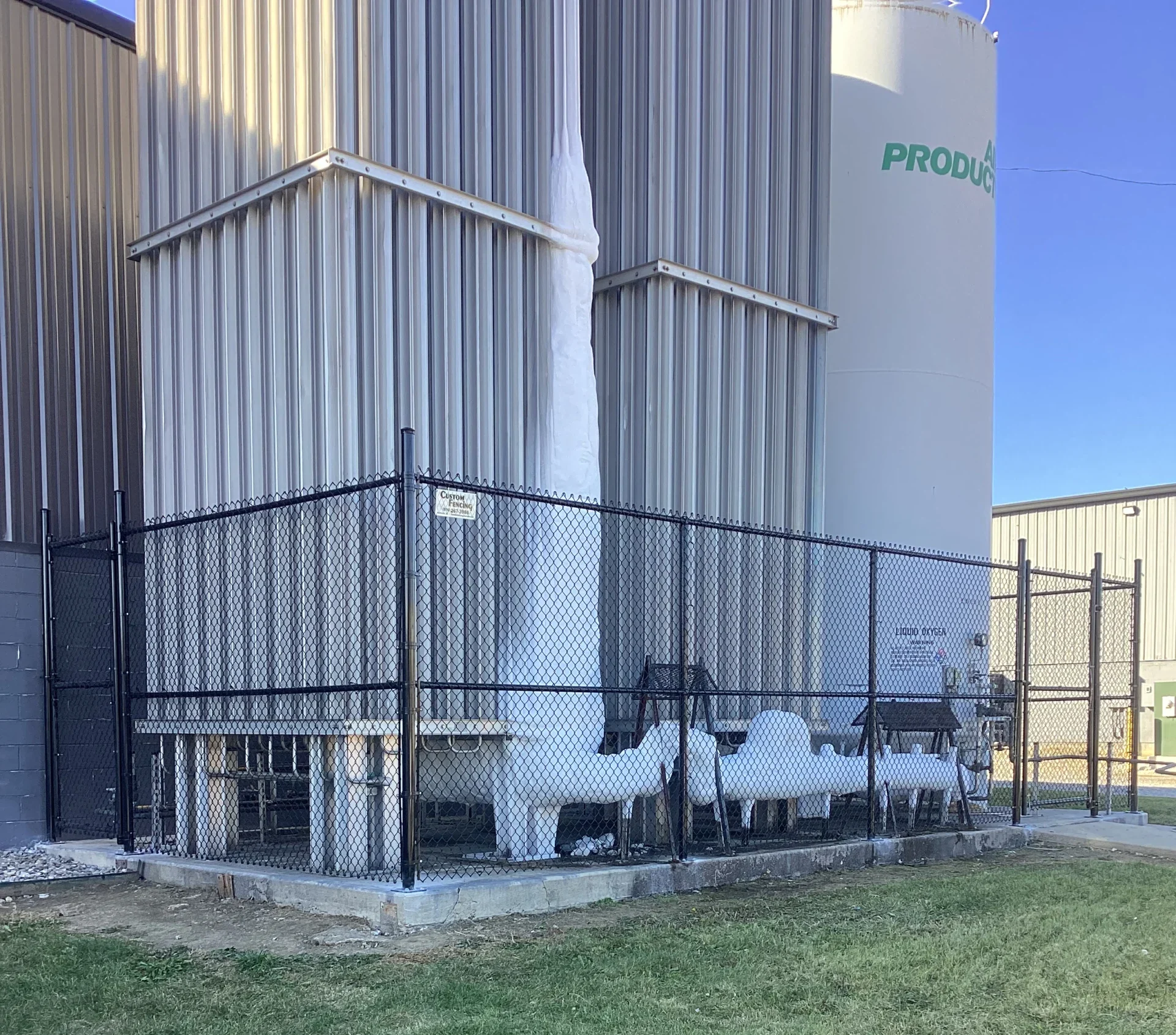 A commercial-grade black vinyl-coated chain-link fence and gate enclosing industrial equipment and tanks