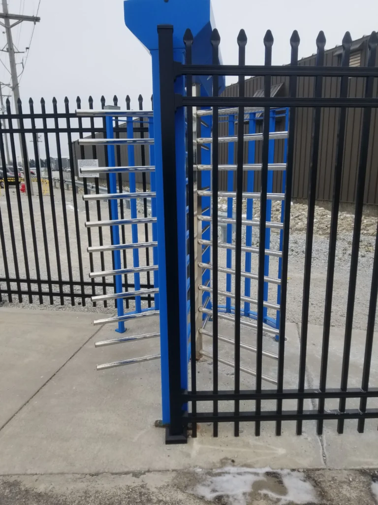 A heavy-duty full-height security turnstile with stainless steel rotating arms integrated into a black ornamental steel fence