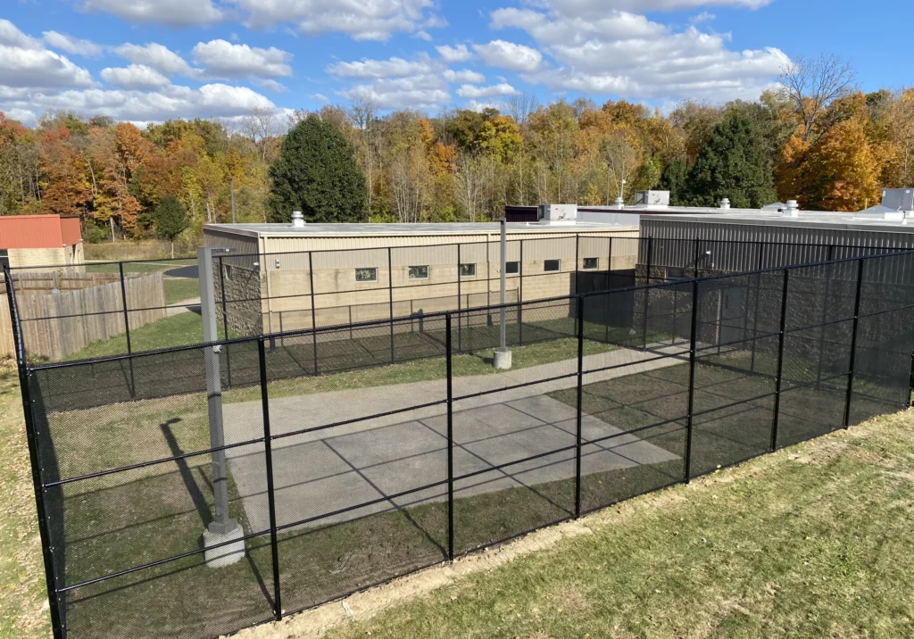 A high-security black vinyl-coated chain-link enclosure with micro-mesh panels surrounding an outdoor recreation area at a commercial facility